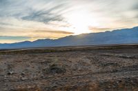 an open plain with the sun peeking over the mountains in the distance and the sun setting on the horizon