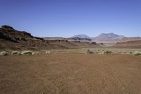 a deserted desert area in the middle of the day with mountains and rocky cliffs in the distance