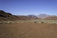 a deserted desert area in the middle of the day with mountains and rocky cliffs in the distance