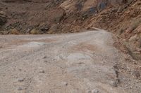 a dirt road leading through some rocky terrain with a small truck on it's right hand side