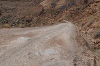 a dirt road leading through some rocky terrain with a small truck on it's right hand side