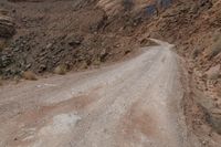 a dirt road leading through some rocky terrain with a small truck on it's right hand side