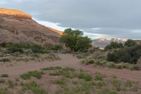 dirt road that leads to a barren rocky hillside with hills in the background and clouds in the sky