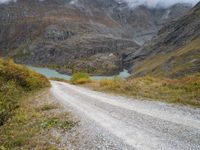 the view of a rocky, mountainous road near a mountain lake with clouds in the sky