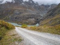 the view of a rocky, mountainous road near a mountain lake with clouds in the sky