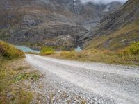 the view of a rocky, mountainous road near a mountain lake with clouds in the sky