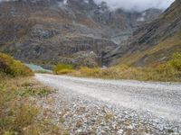 the view of a rocky, mountainous road near a mountain lake with clouds in the sky