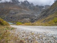 the view of a rocky, mountainous road near a mountain lake with clouds in the sky