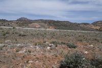 a large arid area with a road and mountains behind it and a blue sky above the ground