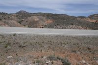 a large arid area with a road and mountains behind it and a blue sky above the ground