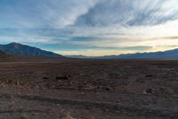 a dirt plain with some mountains and clouds in the sky under blue skies, with a lone person sitting on it