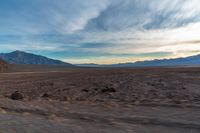 a dirt plain with some mountains and clouds in the sky under blue skies, with a lone person sitting on it