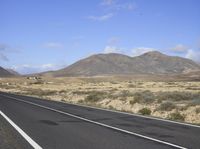 a long highway runs through a desert area with mountains in the distance and clouds overhead