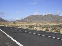 a long highway runs through a desert area with mountains in the distance and clouds overhead