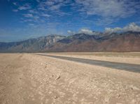 an empty desert road with mountains in the background and water running down it into the middle