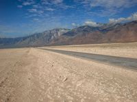 an empty desert road with mountains in the background and water running down it into the middle