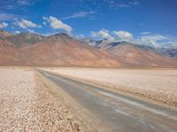 the desert road is surrounded by mountains and clouds in the background with several people on it