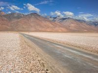 the desert road is surrounded by mountains and clouds in the background with several people on it