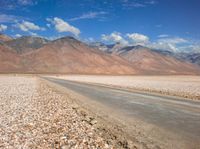 the desert road is surrounded by mountains and clouds in the background with several people on it