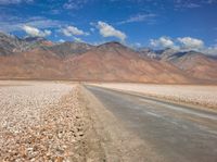 the desert road is surrounded by mountains and clouds in the background with several people on it