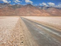 the desert road is surrounded by mountains and clouds in the background with several people on it