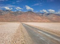 the desert road is surrounded by mountains and clouds in the background with several people on it