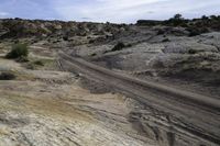 a road with rocks and scruby scrub in the background, and dirt trail in the foreground