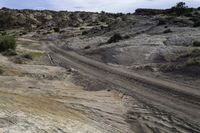 a road with rocks and scruby scrub in the background, and dirt trail in the foreground