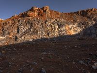 the shadow of a person in front of a rocky surface and a mountain at sunset