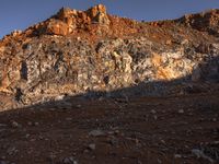 the shadow of a person in front of a rocky surface and a mountain at sunset