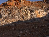 the shadow of a person in front of a rocky surface and a mountain at sunset