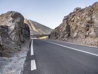 a paved road is near a mountain side and the sky is low in the background