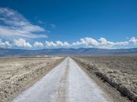 a long dirt road stretches into the distance in a vast desert plain area with mountains in the distance