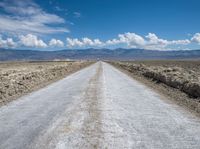 a long dirt road stretches into the distance in a vast desert plain area with mountains in the distance