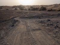 a truck on a dirt road in the desert with rocks and stones on the ground