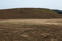 a lone horse that is walking in the middle of an empty field of dirt with mountains behind