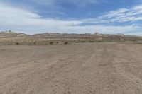 an empty field next to a big mountain with rocks in the background of the picture