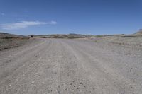 a dirt road is surrounded by some hills and desert like terrain as the vehicle sits on it