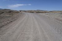 a dirt road is surrounded by some hills and desert like terrain as the vehicle sits on it