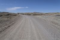 a dirt road is surrounded by some hills and desert like terrain as the vehicle sits on it