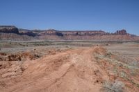 a dirt road through a desert plain with a mountain behind it and a clear blue sky in the background