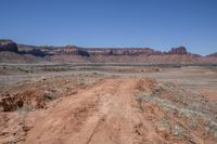 a dirt road through a desert plain with a mountain behind it and a clear blue sky in the background