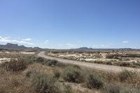 an empty road in a wide open plain of land near mountains and water on a sunny day