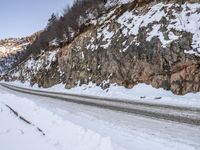 the road has snow and rocks on it by a rocky cliff in winter time on the side