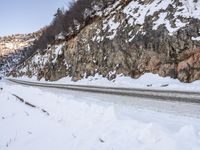 the road has snow and rocks on it by a rocky cliff in winter time on the side