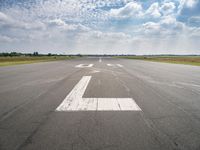 a runway with an airplane landing strip in the middle of it and clouds overhead on the blue sky