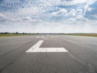 a runway with an airplane landing strip in the middle of it and clouds overhead on the blue sky