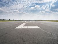 a runway with an airplane landing strip in the middle of it and clouds overhead on the blue sky