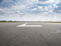 a runway with an airplane landing strip in the middle of it and clouds overhead on the blue sky