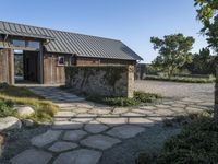 the outside of a rustic house with a walkway through it, a large stone courtyard and two wooden entry doors leading to an open kitchen